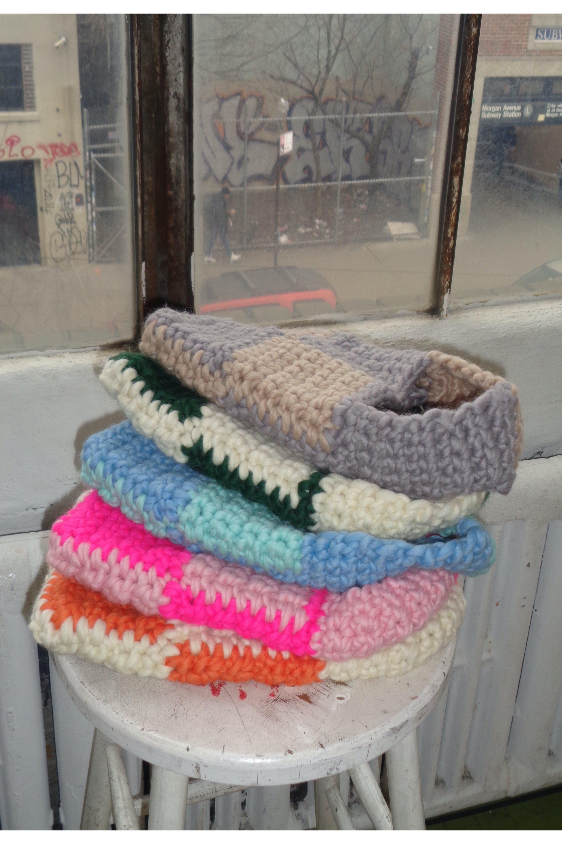 Stack of checkered crochet bags in different colors lying on a white stool.