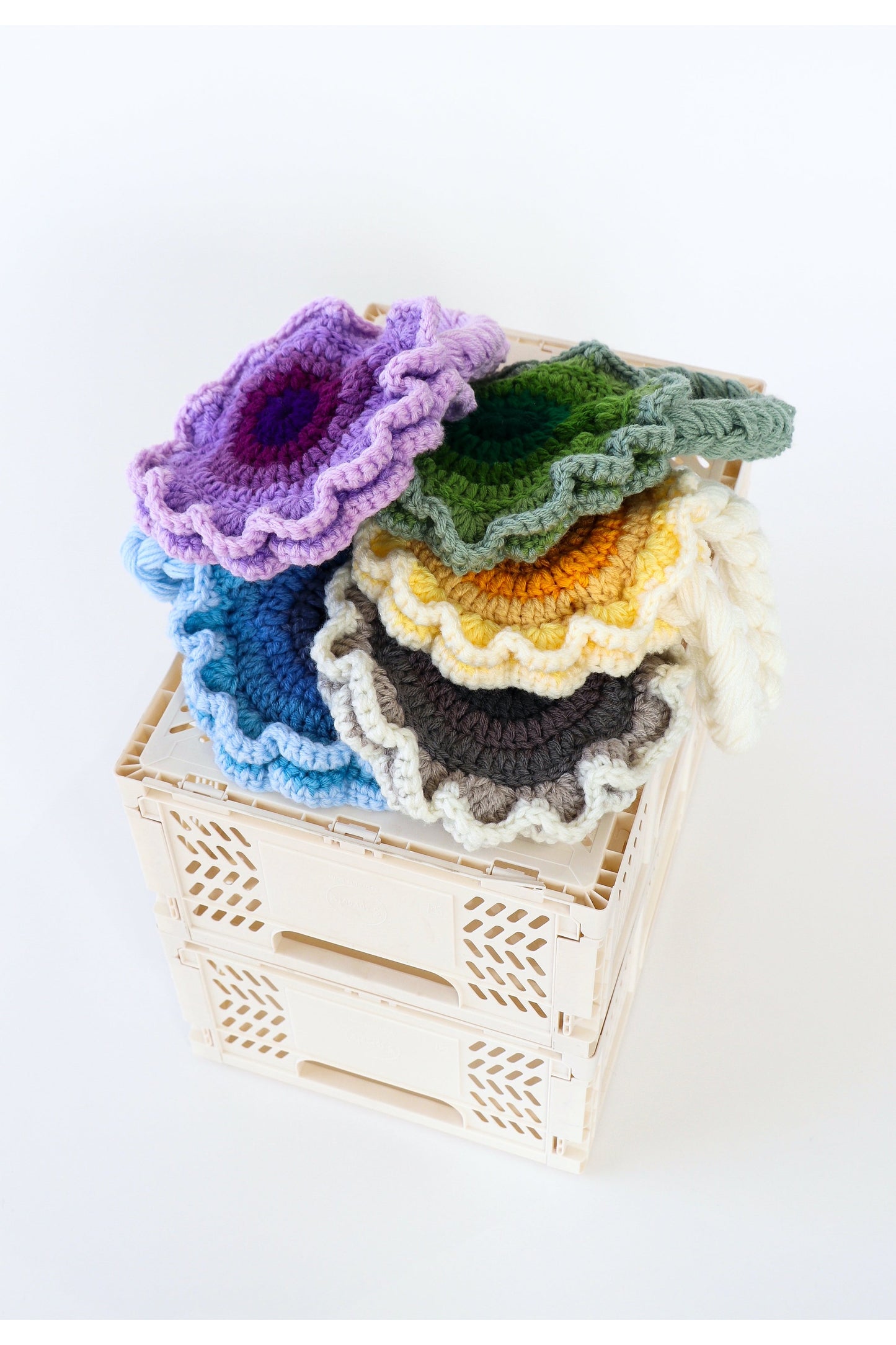 Stack of multicolored flower crochet shoulder bags lying on top of a white milk crate.