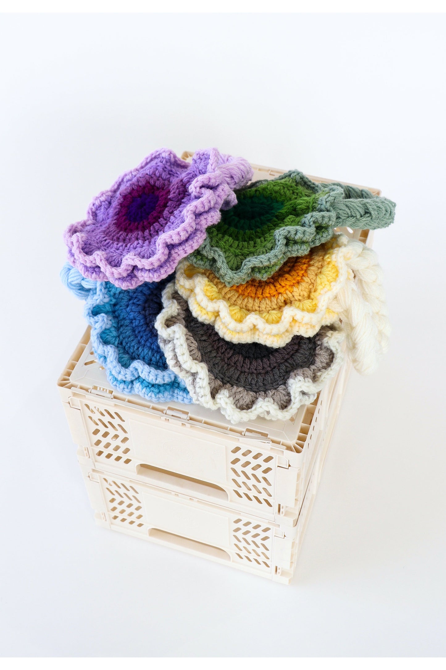 Stack on multicolored flower crochet shoulder bags lying on top of a white milk crate.