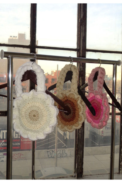 Three flower shaped crochet shoulder bags in different colors hanging on a clothing rack.