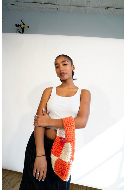 Model wearing orange and cream checkered crochet bag on her arm.