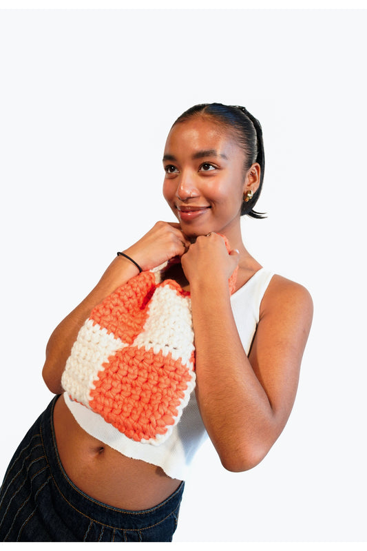 Model holding an orange and cream checkered crochet shoulder bag.